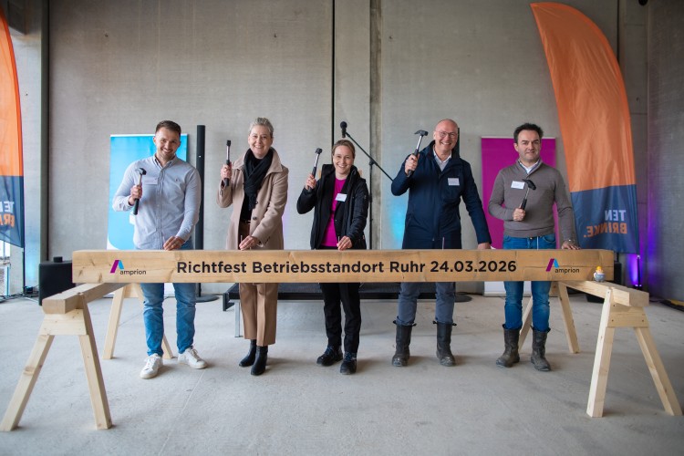 Fünf Personen mit Hämmern beim Richtfest des Amprion-Betriebsstandorts Ruhr am 24. März 2026; im Vordergrund ein Holzbalken mit der Aufschrift Richtfest Betriebsstandort Ruhr 24.03.2026.