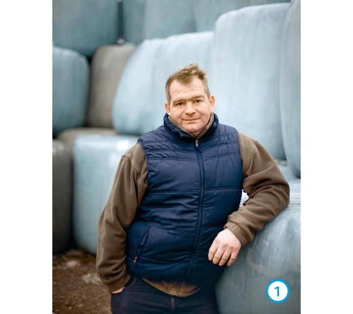 Das Bild zeigt Landwirt Herrmann Westermann. Er lehnt an einen Rundballen und trägt eine blaue Weste über einem braunen Pullover