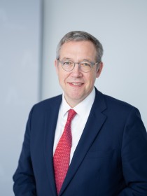 Dr. Christoph Müller, Mitglied der Amprion-Geschäftsführung ab Juli 2024 und Vorsitzende der AmprionGeschäftsführung ab 1. Januar 2025, steht in Geschäftskleidung in einem hellen Raum. Auf der Wand hinter ihm ist das Logo der Amprion GmbH erkennbar.