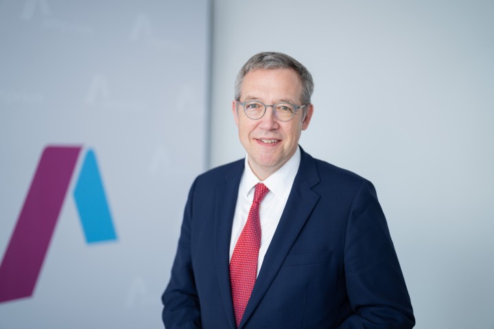 Dr. Christoph Müller, Mitglied der Amprion-Geschäftsführung ab Juli 2024 und Vorsitzende der AmprionGeschäftsführung ab 1. Januar 2025, steht in Geschäftskleidung in einem hellen Raum. Auf der Wand hinter ihm ist das Logo der Amprion GmbH erkennbar.