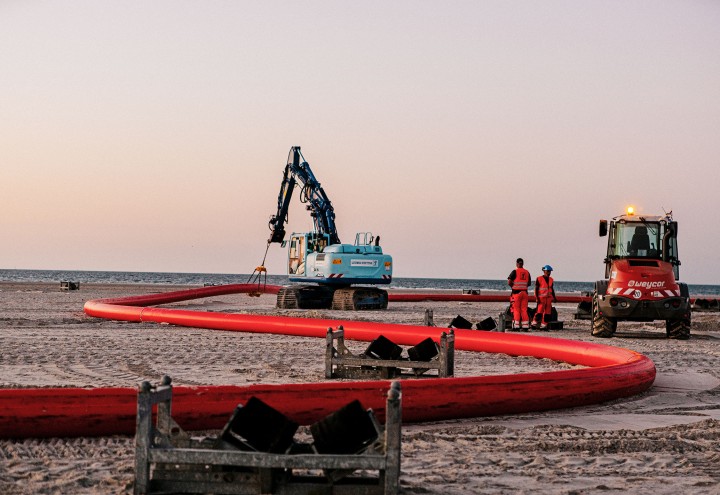 Baustelle auf Norderney mit roten Rohren, zwei Arbeitern, einem roten und einem hellblauen Bagger