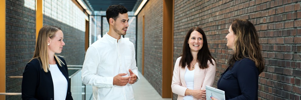 Vier Amprion-Mitarbeitende im Gespräch in einem modernen Büroflur mit Backsteinwand. 
