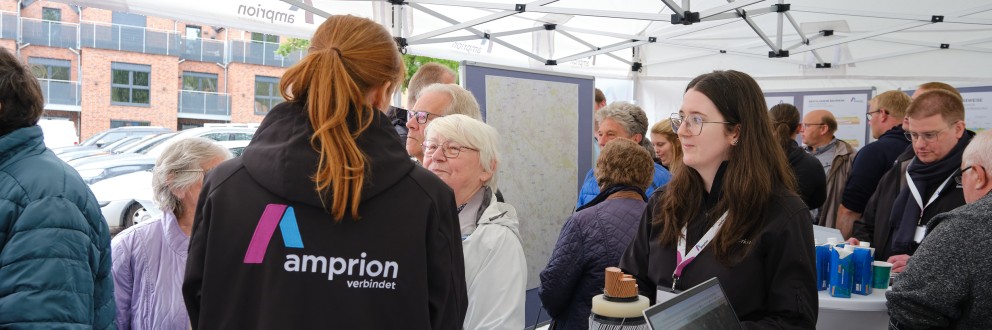 Mitarbeitende von Amprion im Gespräch mit Bürgerinnen und Bürgern an einem Informationsstand in einem weißen Zelt.