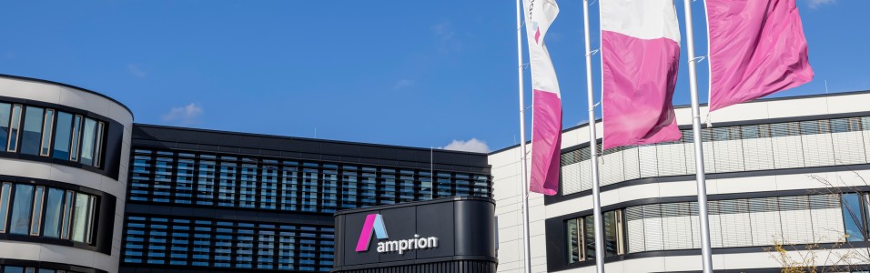 Amprion-Firmensitz mit drei wehenden Amprion-Fahnen vor dem Eingangsgebäude bei blauem Himmel. 
