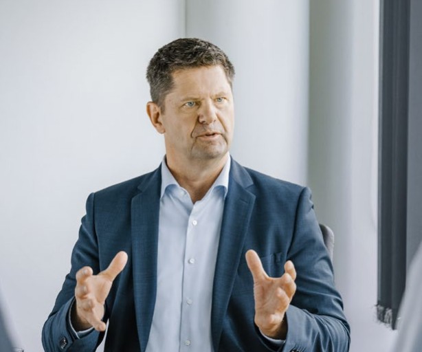 Das Bild zeigt den CFO der Amprion GmbH, Herrn Peter Rüth. Herr Rüth sitzt in einem Büro, vor ihm ein paar Unterlagen. Herr Rüth trägt ein dunkles Sakko über einem hellblauen Hemd ohne Krawatte. Er blickt den interviewenden an. Es ist eine klassische interviewsituation. 