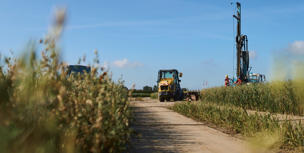 Ein Bagger und ein Bohrer am Ende einer Baustraße auf einem Feld.