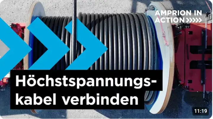 Das Bild ist ein Screenshot aus einem Video der Amprion-Reihe "Amprion in Action" und zeigt den Kabeleinzug auf einer Baustelle für die Energiewende-Trasse A-Nord. Im Vordergrund dominiert eine große, mit schwarzem Kabel umwickelte Trommel, die auf einem roten Gestell montiert ist. Der Text im Bild lautet "Höchstspannungs-kabel verbinden" und "AMPRION IN ACTION". 