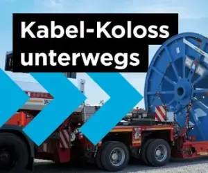 Das Bild, ein Screenshot aus der Videoreihe "AMPRION IN ACTION", zeigt einen Lastkraftwagen, der eine überdimensionale, blaue Kabeltrommel auf einem roten Tieflader transportiert. Die Trommel enthält das Erdkabel, das für die etwa 300 Kilometer lange Gleichstromverbindung A-Nord von Emden nach Osterath benötigt wird. Der Text im Bild lautet: "Kabel-Koloss unterwegs" und "AMPRION IN ACTION". Der Transport von diesen bis zu 35 Tonnen schweren Trommeln erfolgt im Rahmen der Logistik für dieses zentrale Energiewende-Projekt. 