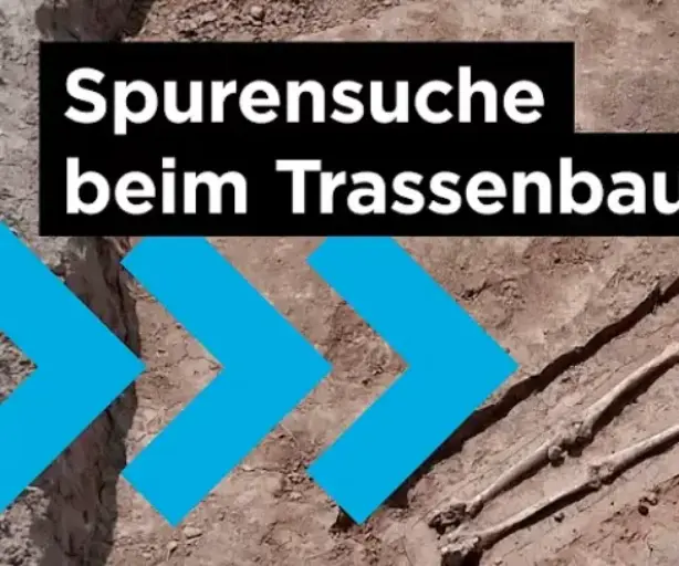 Das Bild ist ein Screenshot aus einem Video und zeigt eine Nahaufnahme eines vollständig freigelegten menschlichen Skeletts, das in einer archäologischen Grabungsfläche im lockeren Erdreich liegt. Der Fund wurde im Rahmen von Voruntersuchungen für den Bau der Amprion-Erdkabeltrasse A-Nord gemacht, wie der Text im Bild "Spurensuche beim Trassenbau" und "AMPRION IN ACTION" angibt. 