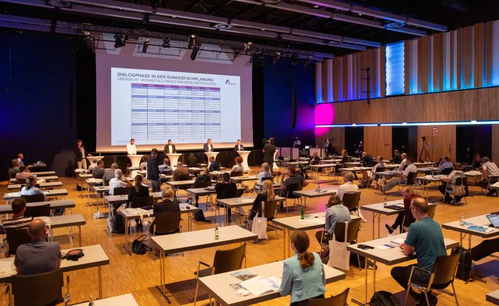 Große Konferenz zu Dialogphasen in der Bundesfachplanung mit Präsentationstafel und Teilnehmenden.
