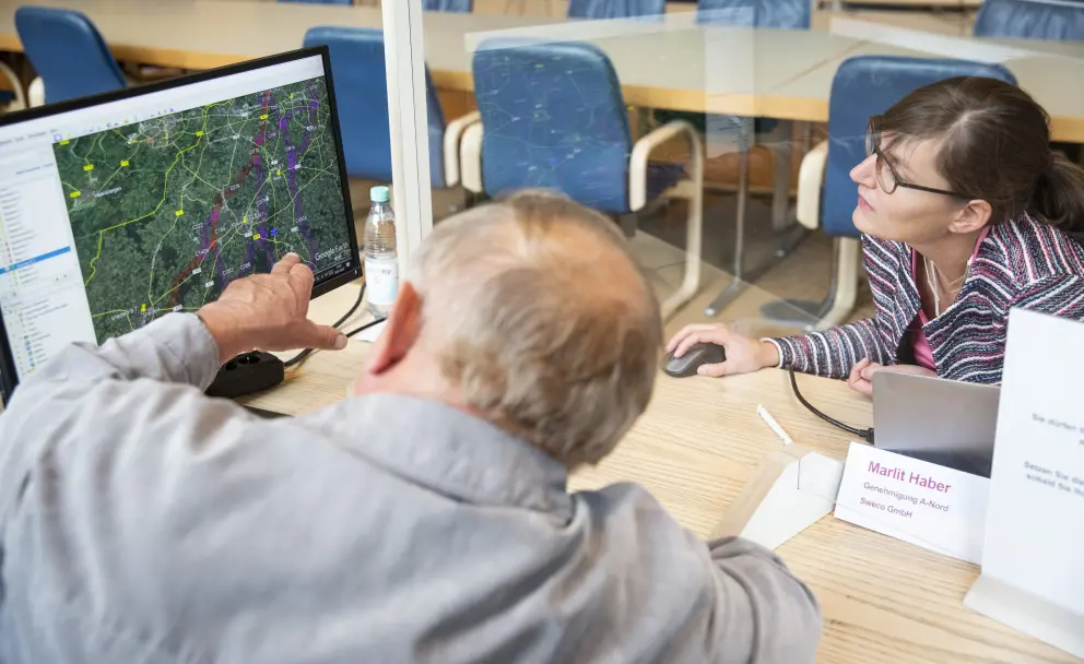 Mann zeigt Frau auf Computermonitor eine Karte mit markiertem Trassenverlau