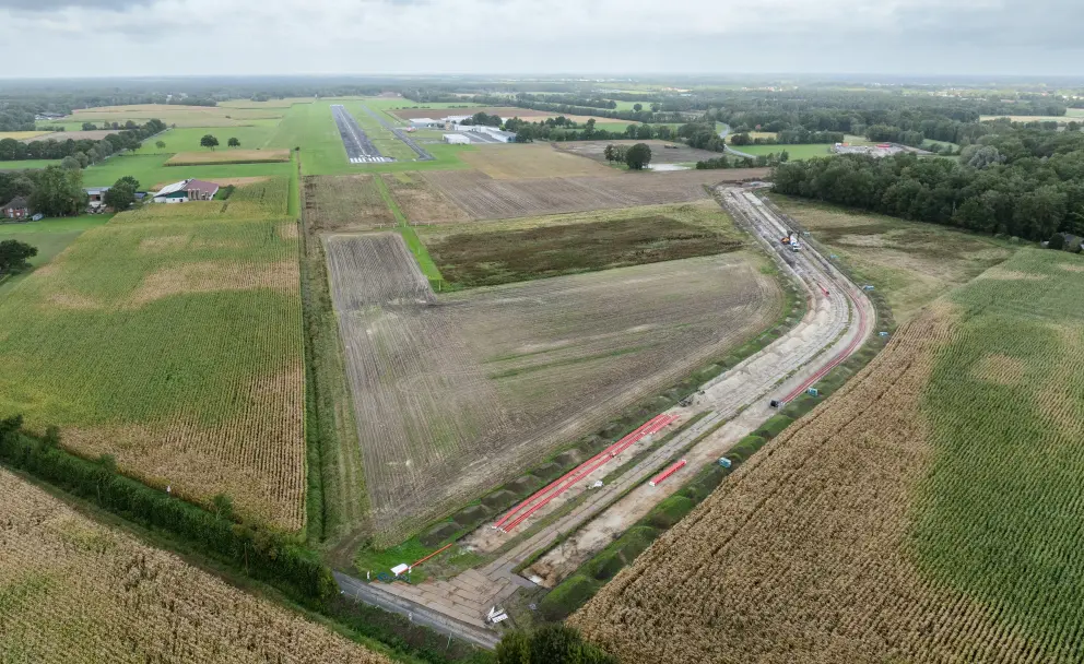 Luftaufnahme eines offenen Grabens für Erdkabel, der durch Ackerland neben einem Flugplatz führt.
