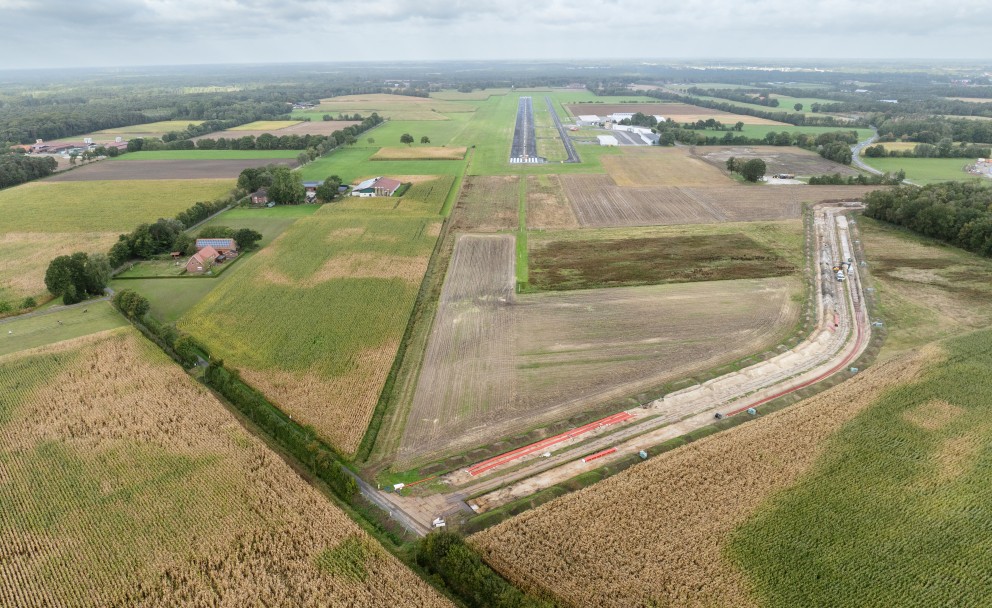 Luftaufnahme einer Baustelle für einen offenen Graben, der durch Ackerland neben einem Flugplatz führt.
