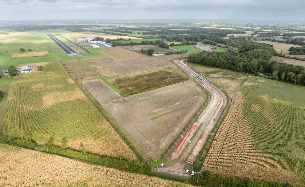 Luftaufnahme eines offenen Grabens für Erdkabel, der durch Ackerland neben einem Flugplatz führt.