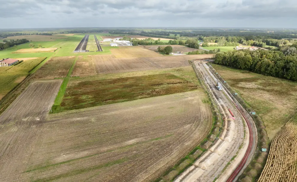 Luftaufnahme eines offenen Grabens für Erdkabel, der durch Ackerland neben einem Flugplatz führt.
