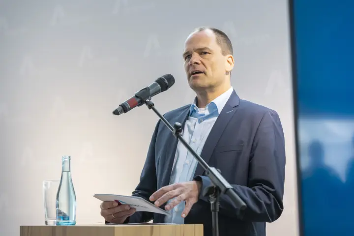 Mann im Anzug spricht am Rednerpult in ein Mikrofon.