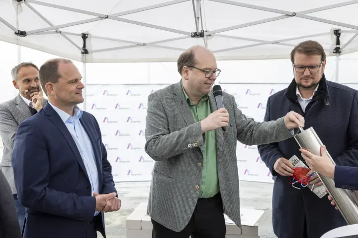 Drei Männer bei einer Zeremonie, bei der etwas in ein Metallrohr gelegt wird.