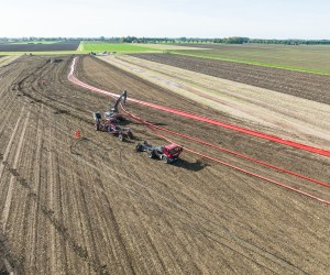 Landwirtschaftliches Feld mit zwei Fahrzeugen, die an einem Kabelpflug arbeiten, und roten Kabeln, die über das Feld verlaufen