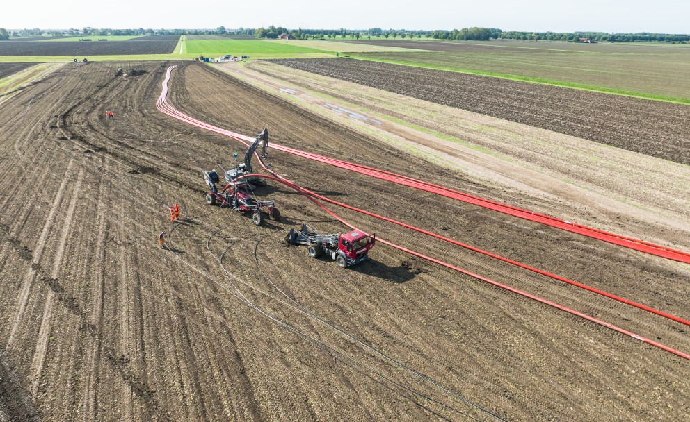 Landwirtschaftliches Feld mit zwei Fahrzeugen, die an einem Kabelpflug arbeiten, und roten Kabeln, die über das Feld verlaufen