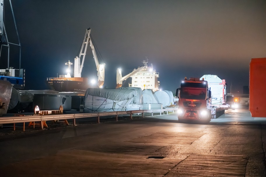 Nachtaufnahme eines Hafens mit beleuchtetem Frachtschiff, großen verpackten Gütern und einem Lkw auf der Straße