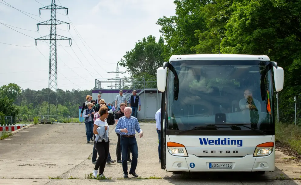Eine Gruppe von Menschen steigt aus einem weißen Reisebus der Marke Setra mit der Aufschrift 'Wedding' aus.