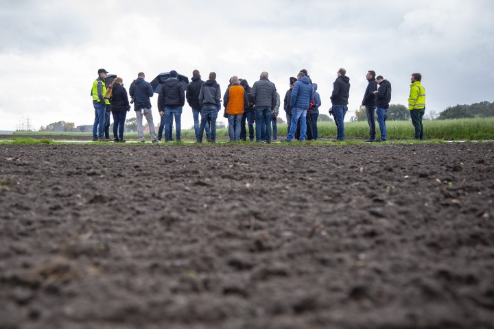 Gruppe von Menschen steht auf einem Acker unter bewölktem Himmel, einige tragen gelbe Warnwesten.
