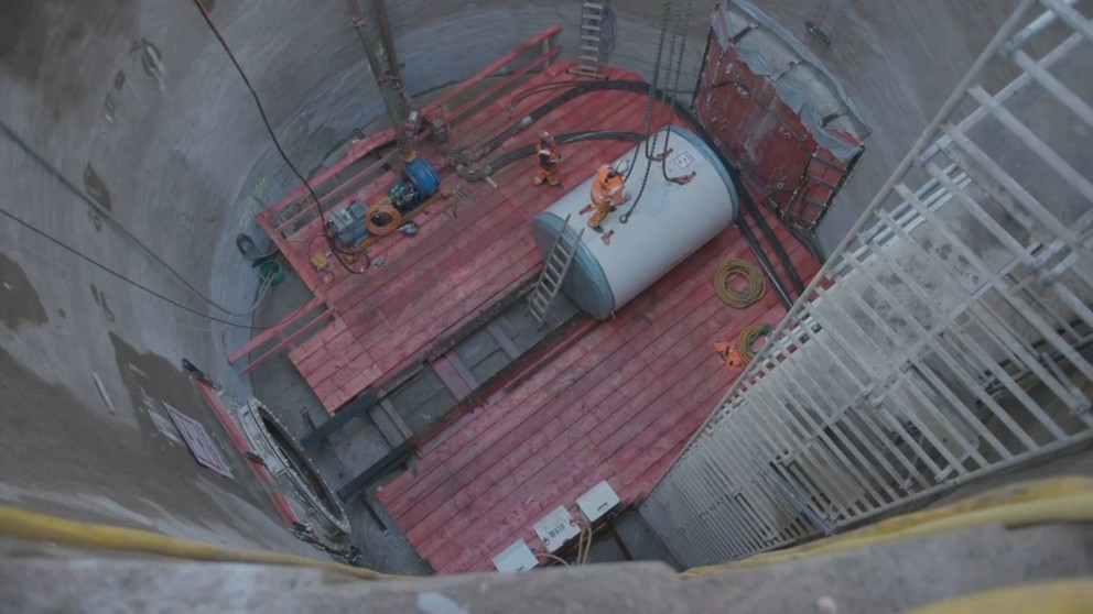 Das Bild zeigt einen Teil der rot/weißen Tunnelbohrmaschine in einem Betonschacht.