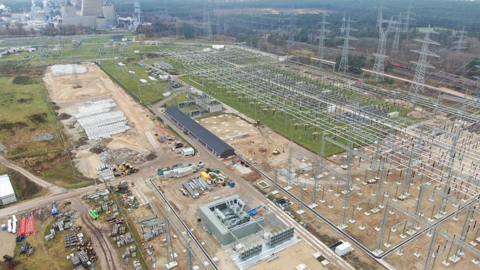 Das Bild ist eine erhöhte Luftaufnahme oder Drohnenansicht einer sehr großen und weitläufigen Industrieanlage, die primär aus einem Hochspannungs-Umspannwerk besteht. Der Himmel ist bewölkt und das Licht ist diffus, was auf einen bedeckten Tag hindeutet.