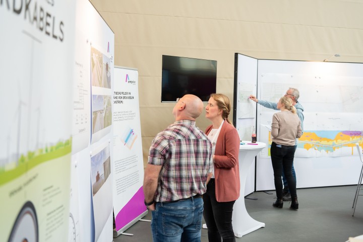 Informationsveranstaltung: Zwei Personen stehen im Vordergrund vor einer aufgebauten Wand mit Bildern, im Hintergrund stehen noch zwei weitere Personen vor einer anderen Wand. 