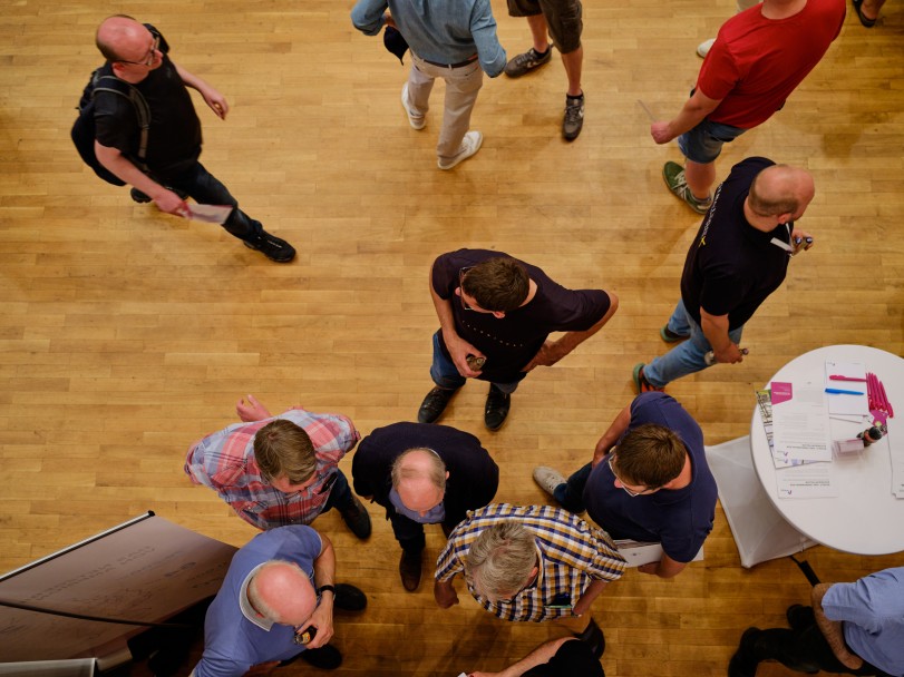 Infoveranstaltung von oben: Viele verschiedene Menschen stehen oder gehen umher und schauen sich um.