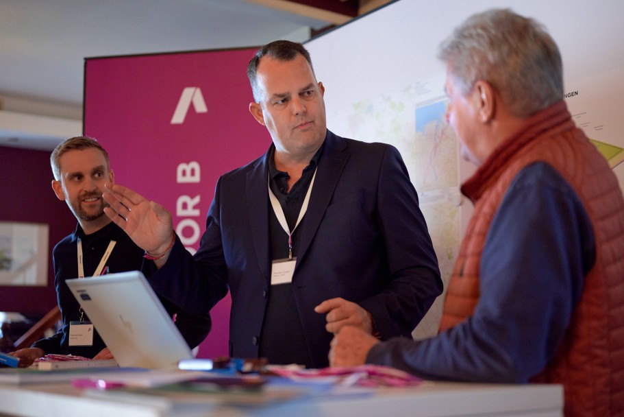 (c) Tennet/Timo Wilke
Drei Personen stehen an einem Tisch, auf dem ein Laptop steht. Die Person in der Mitte gestikuliert mit den Händen und blickt dabei in die Richtung einer Person, die seitlich zur Kamera steht.