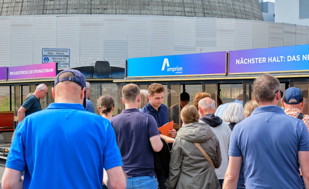 Eine Besuchergruppe versammelt sich vor einer Bimmelbahn mit Amprion-Bandenwerbung, während ein Mitarbeiter mit einer Klemmmappe Dokumente verteilt.