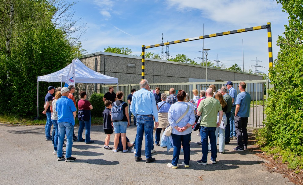 Eine größere Besuchergruppe versammelt sich unter blauem Himmel vor einem betonierten Betriebsgebäude und einem weißen Pavillonzelt bei einer Amprion-Führung.