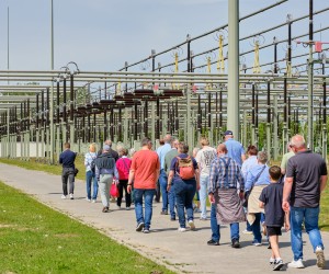 Gruppe von Menschen geht auf einem Weg neben einer großen Anlage mit vielen Metallstreben und Drähten
