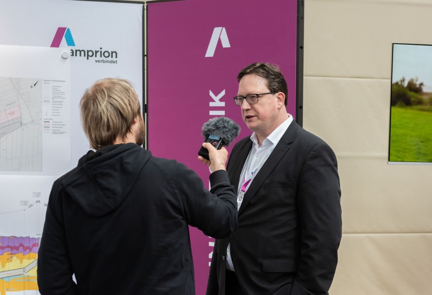 Zwei Männer im Interview: Die zur Kamera mit dem Rücken gerichtete Person hält dem Mann im Anzug ein Mikrofon vor den Mund.