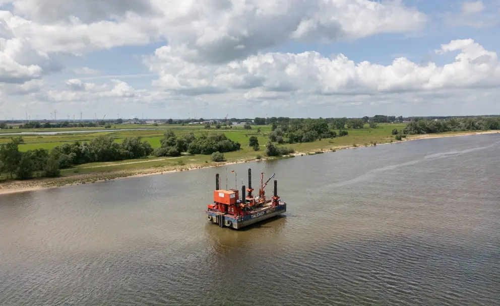 Eine orange-rote Arbeitsplattform, genutzt für Baugrunduntersuchungen, verankert auf einem breiten Fluss.
