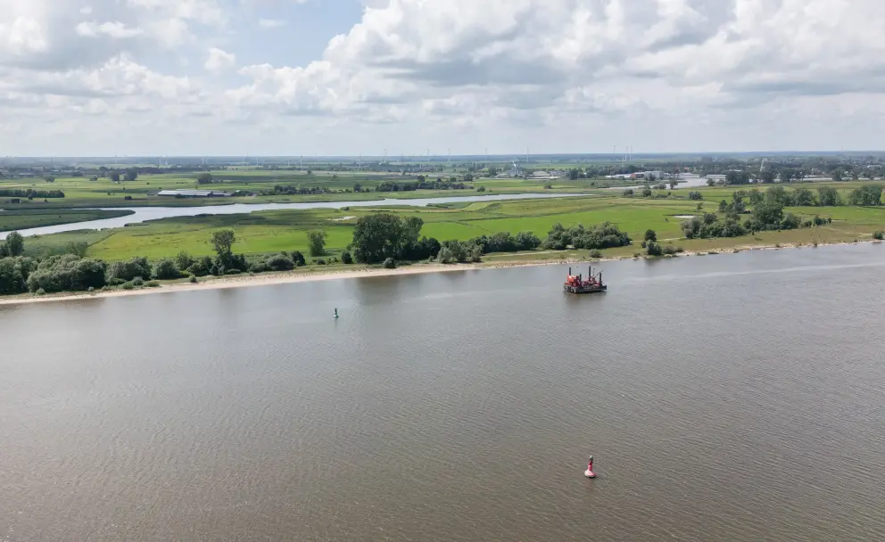 Luftaufnahme einer weiten Flusslandschaft mit einer schwimmenden orange-roten Arbeitsplattform in der Ferne.