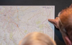 Das Bild zeigt eine Nahaufnahme, aus der Vogelperspektive aufgenommen, von einer Person, die sich über ein aufgeschlagenes Planungsdokument mit einer komplexen Landkarte beugt. Die Karte selbst ist ein typisches Planungsinstrument, das bei der Erörterung von Infrastrukturprojekten wie neuen Strom- oder Verkehrstrassen verwendet wird. 