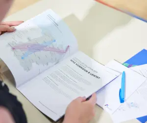 Das Bild zeigt eine Nahaufnahme, aus der Vogelperspektive aufgenommen, von einer Person, die sich über ein aufgeschlagenes Planungsdokument mit einer komplexen Landkarte beugt.