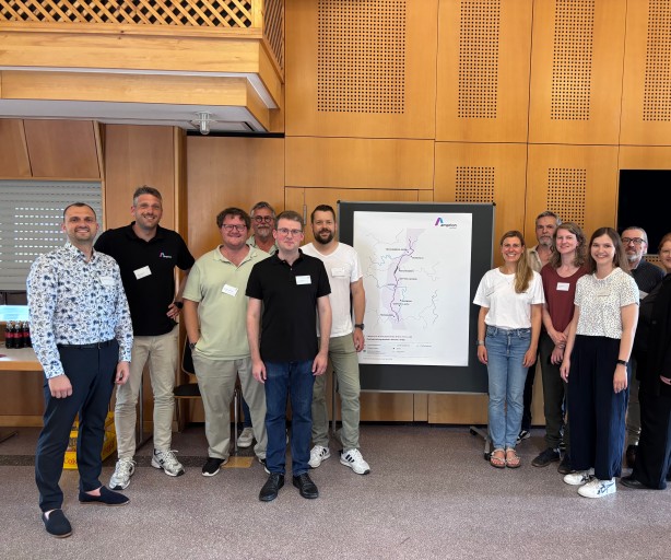 Gruppe von elf Personen steht vor einer Wand mit einem großen Amprion Plakat, das eine schematische Karte zeigt, alle tragen Namensschilder und lächeln in die Kamera