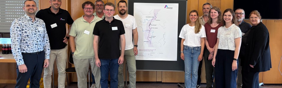 Gruppe von elf Personen steht vor einer Wand mit einem großen Amprion Plakat, das eine schematische Karte zeigt, alle tragen Namensschilder und lächeln in die Kamera
