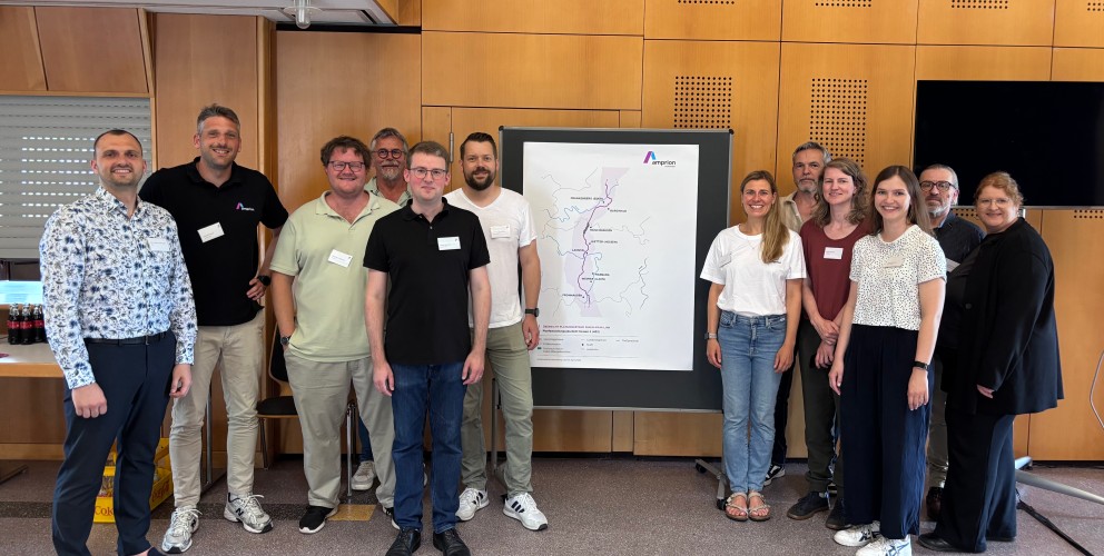 Gruppe von elf Personen steht vor einer Wand mit einem großen Amprion Plakat, das eine schematische Karte zeigt, alle tragen Namensschilder und lächeln in die Kamera