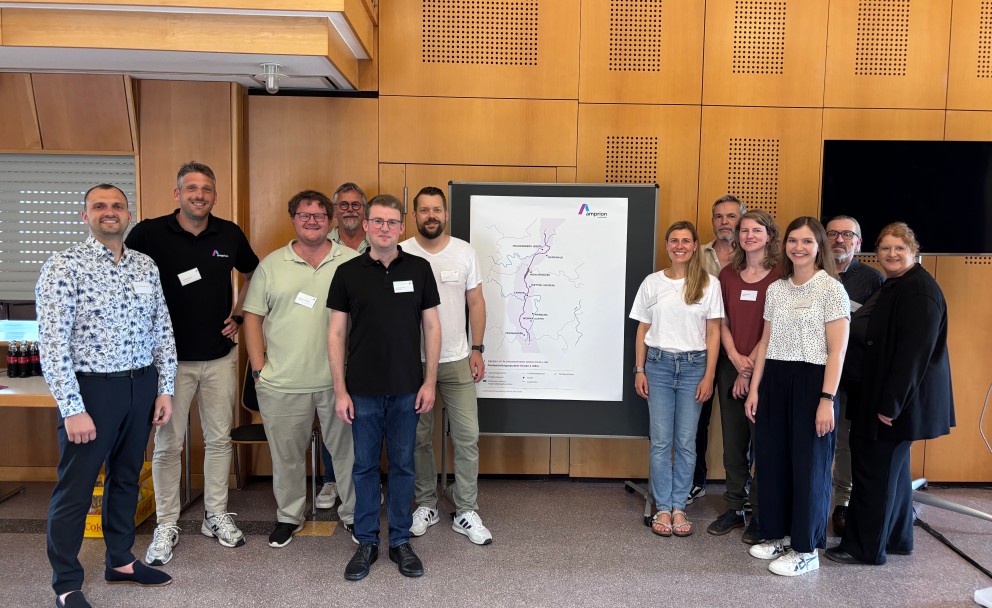 Gruppe von elf Personen steht vor einer Wand mit einem großen Amprion Plakat, das eine schematische Karte zeigt, alle tragen Namensschilder und lächeln in die Kamera