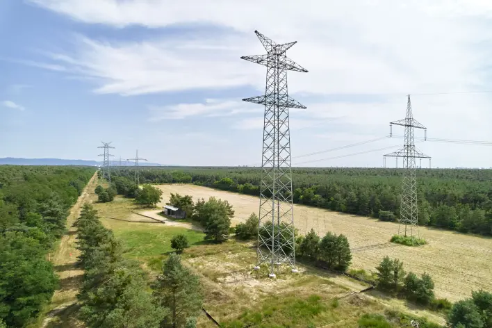 Drohnenaufnahme einer Leitungstrasse bei Lampertheim/Bürstadt: Ein neuer Tonnenmast steht in einer Waldschneise zwischen Kiefernwäldern. In der Ferne verlaufen weitere Masten der Ultranet-Trasse durch die bewaldete Schneise.
