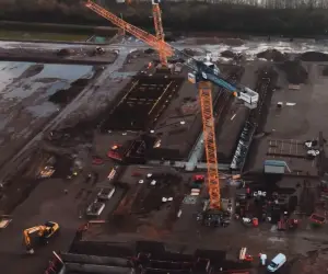 Luftaufnahme der Ultranet-Konverterstandort-Baustelle in der Hochbauphase: orangefarbener Turmdrehkran, Fundamentstrukturen und Baufahrzeuge auf weitläufigem Baufeld.