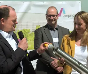 Vier Personen bei der Grundsteinlegung des Ultranet-Konverters; eine spricht in ein Mikrofon, eine weitere hält einen zylindrischen Gegenstand; Amprion-Logo im Hintergrund.