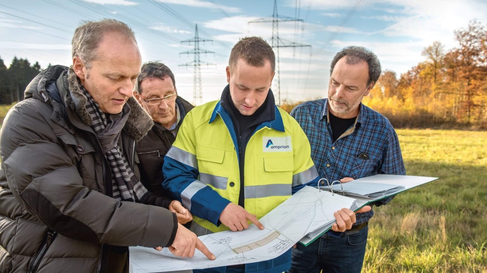 Es folgt eine Bildbeschreibung:
Das Foto im Querformat zeigt vier Herren über eine Karte gebäugt. Das Bild ist Draußen unterhalb einer Stromtrasse entstanden und vermittelt einen freundlichen Eindruck.
Ende der Bildbeschreibung.