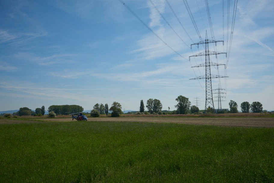 Das Bild zeigt einen gelandeten, blauen Helikopter neben einer Trasse.