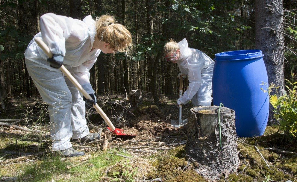 Auf dem Bild sind zwei Frauen mit Schaufeln zu sehen, die die Ameisen in blaue Tonnen übersetzen