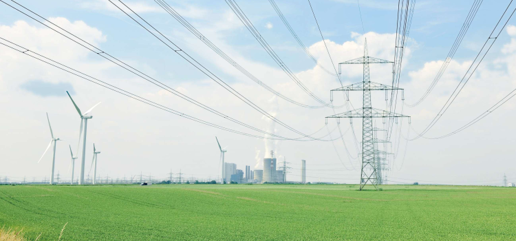 Das Bild zeigt eine Stromtrasse und Windräder in einem grünen Feld - im Hintergrund ein Kraftwerk